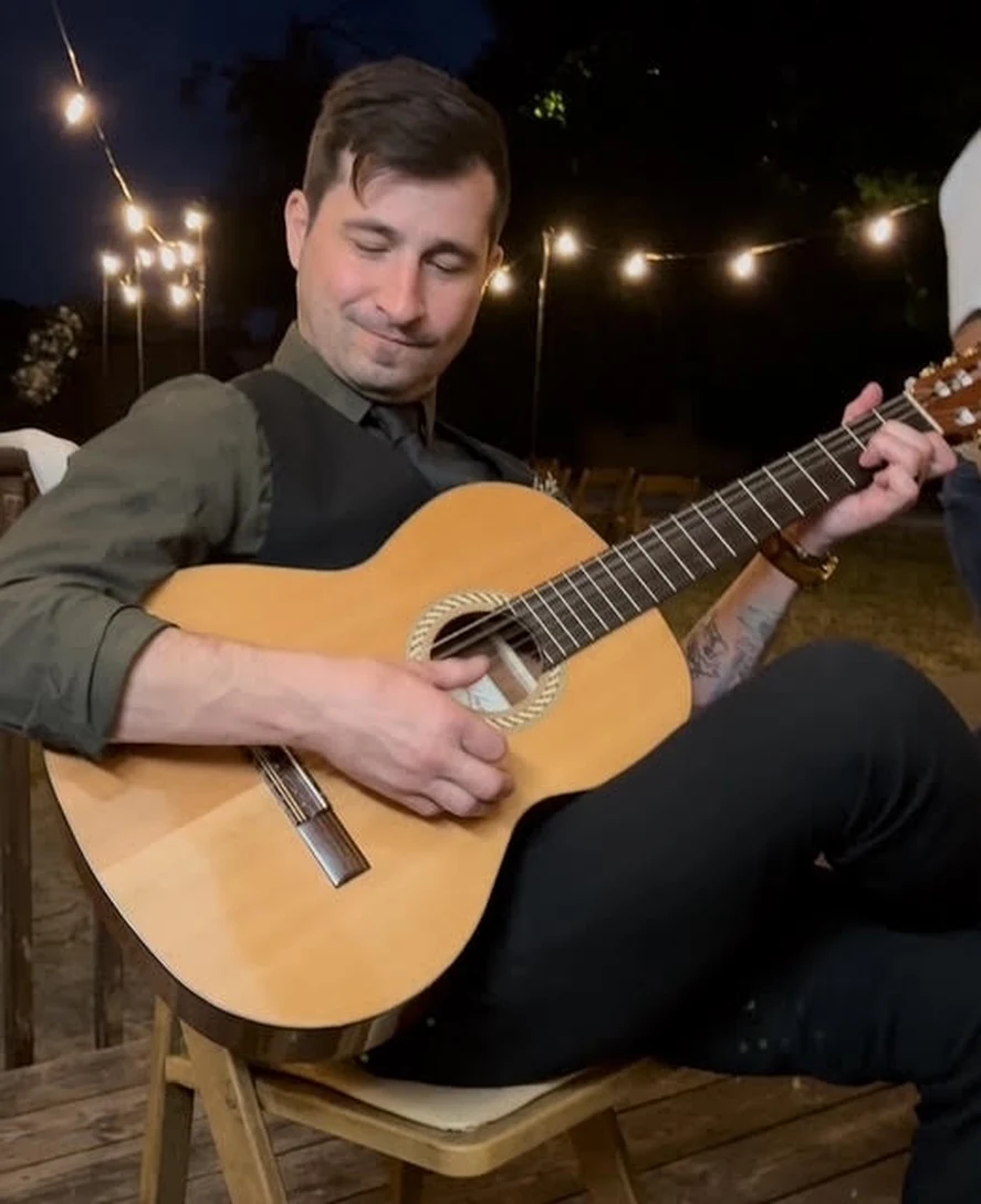 Chad playing a classical guitar outdoors under string lights