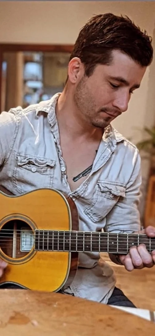 Chad playing an acoustic guitar at a wooden table in a warmly lit room